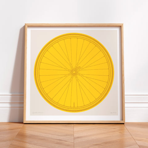 This picture of a contemporary cycling art print features a colourful illustration of a bicycle wheel in tour yellow, beneath it in a hand-written font is the phrase: Spokes Person. The print is framed in a simple oak frame and is sat on a wooden herringbone style floor and leaning against a white wall.