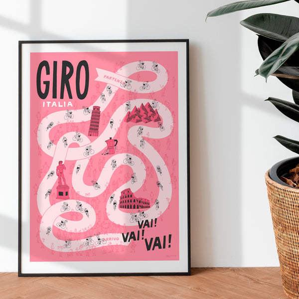 Framed poster of 'Giro Italia' design on a pink background with black text, placed on a wooden surface.