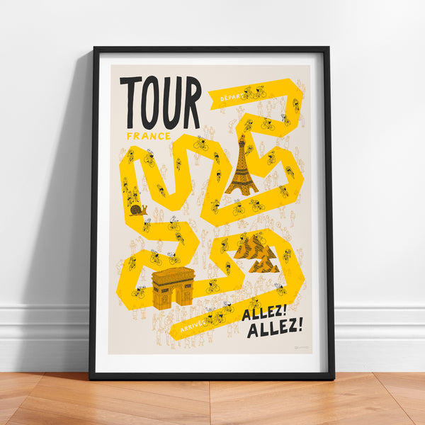 Framed poster of 'Tour de France' with yellow route design and black typography propped up against a white wall.