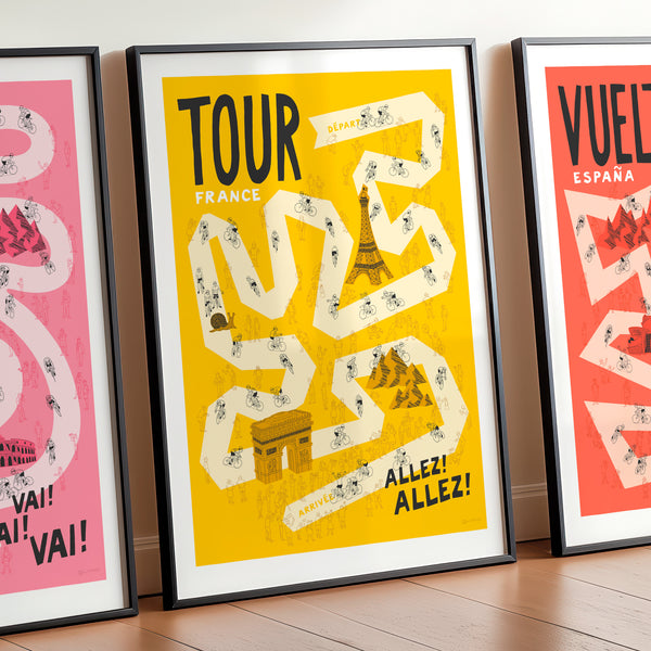 Set of three Grand Tour cycling posters, The Giro, Tour, and Vuelta, focusing on the Tour design with the Giro and Vuelta designs shown cropped off on either side. The print is framed and leaning against a wall and features hand drawn cyclists, bike fans and famous French landmarks, on a pale yellow road set against a darker yellow background. 