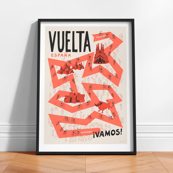 Framed 'Vuelta Espana' poster illustrated with cyclists, fans and famous Spanish landmarks, propped against a white wall.
