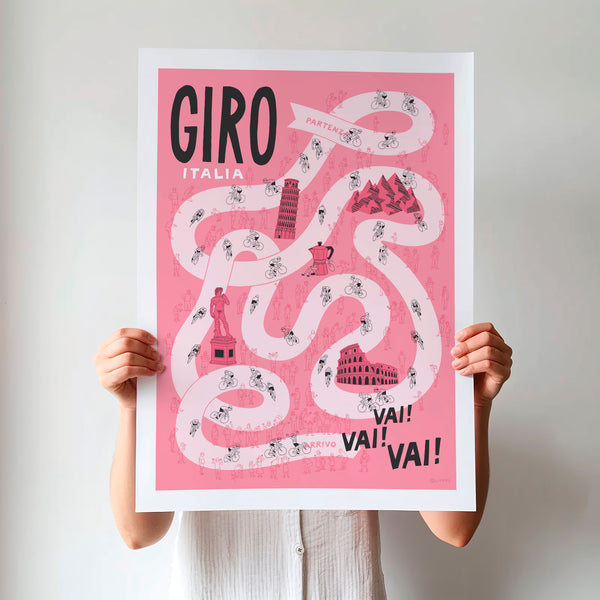 Unframed Giro Grand Tour cycling poster being held up, featuring a pale pink winding road on a darker pink background, including hand drawn illustrations of riders, fans and a selection of famous Italian landmarks.