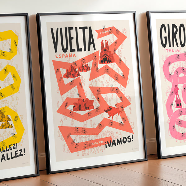 Three framed cycling Grand Tour posters with stylish illustrated designs and bold typography on a wooden floor.