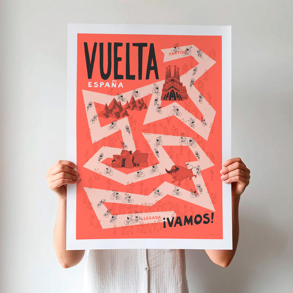 Unframed Vuelta Grand Tour cycling poster being held up, featuring a pale red road on a darker red background, with hand drawn illustrations of cyclists, fans and famous Spanish landmarks.