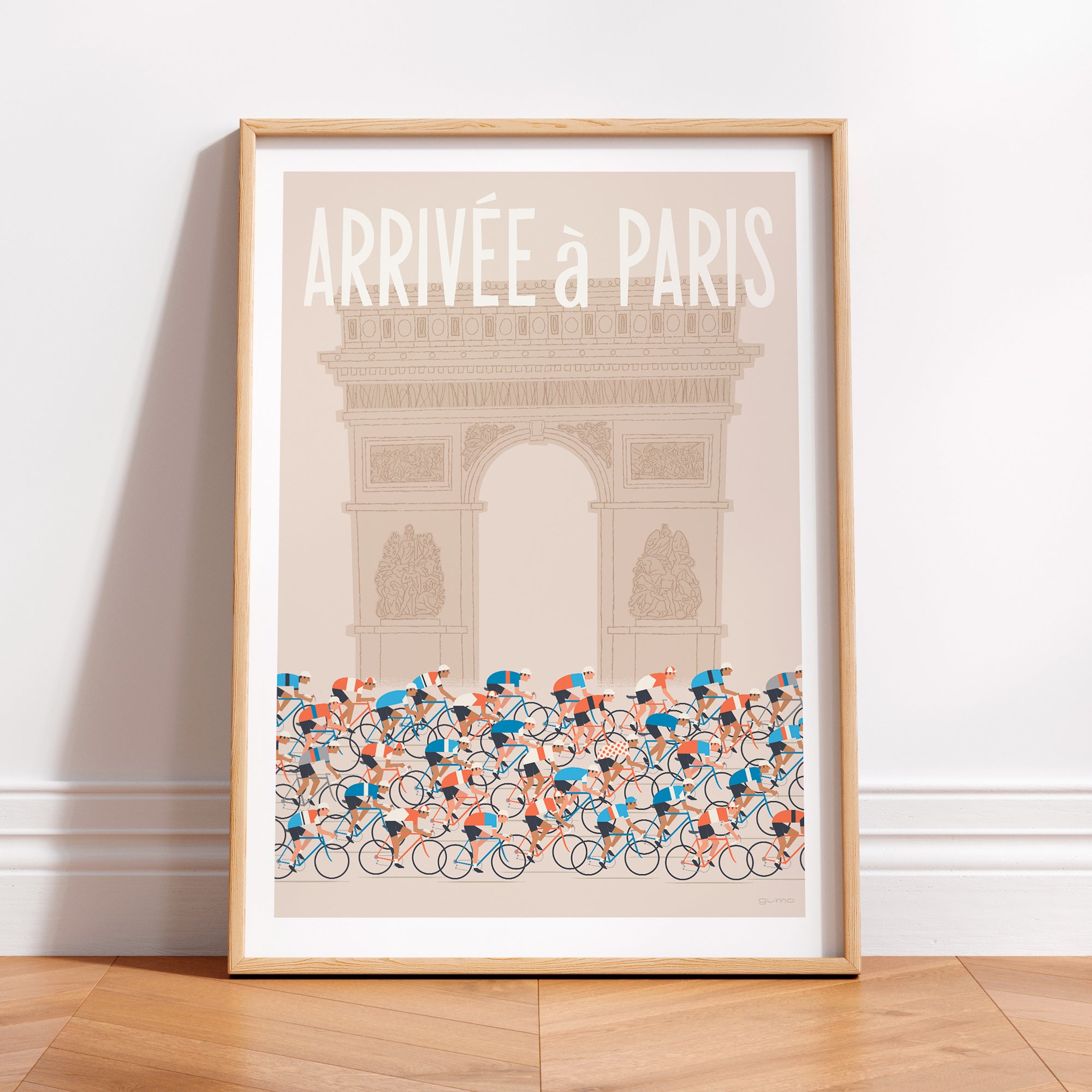 This is a photo of a contemporary style cycling art print in ecru, the poster features a peloton riding past the Arc de Triomphe in Paris, with the words 'Arrivee a Paris' in a white modern font displayed above the Arc. The print is framed in a plain oak frame and is sat on a wooden floor and leaning against a white wall.