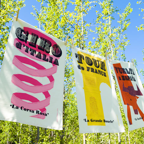 Cycling Grand Tour set of 3 natural cotton tea towels: Tour de France, Giro d'Italia, and Vuelta a Espana, hanging on a washing line outside.